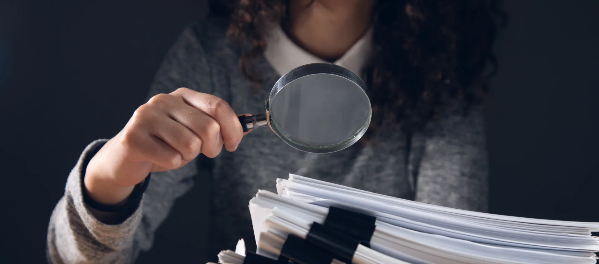 Magnifying glass hovering over a stack of documents and resumes